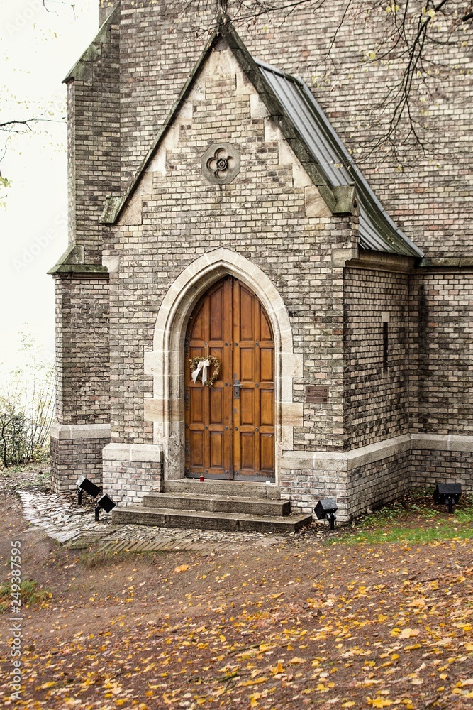 Closed woooden door to Christian chapel in Gothic style.Chapel with large decorated stained-glass windows and a pointed roof.