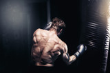 Strong and muscular guy practicing punching the boxing bag. Moody environment. Edgy edit style.