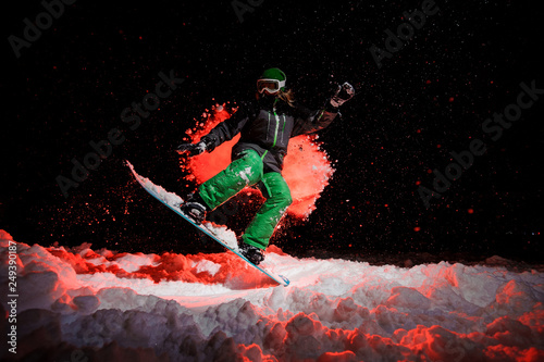 Snowboarder girl dressed in a green sportswear jumping on the mountain hill
