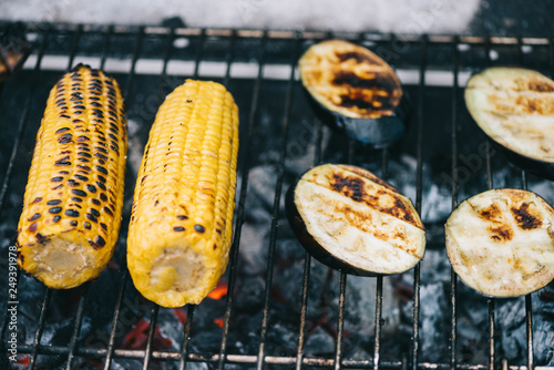 selective focus of yellow corn with crust and eggplant slices grilling on barbecue grid