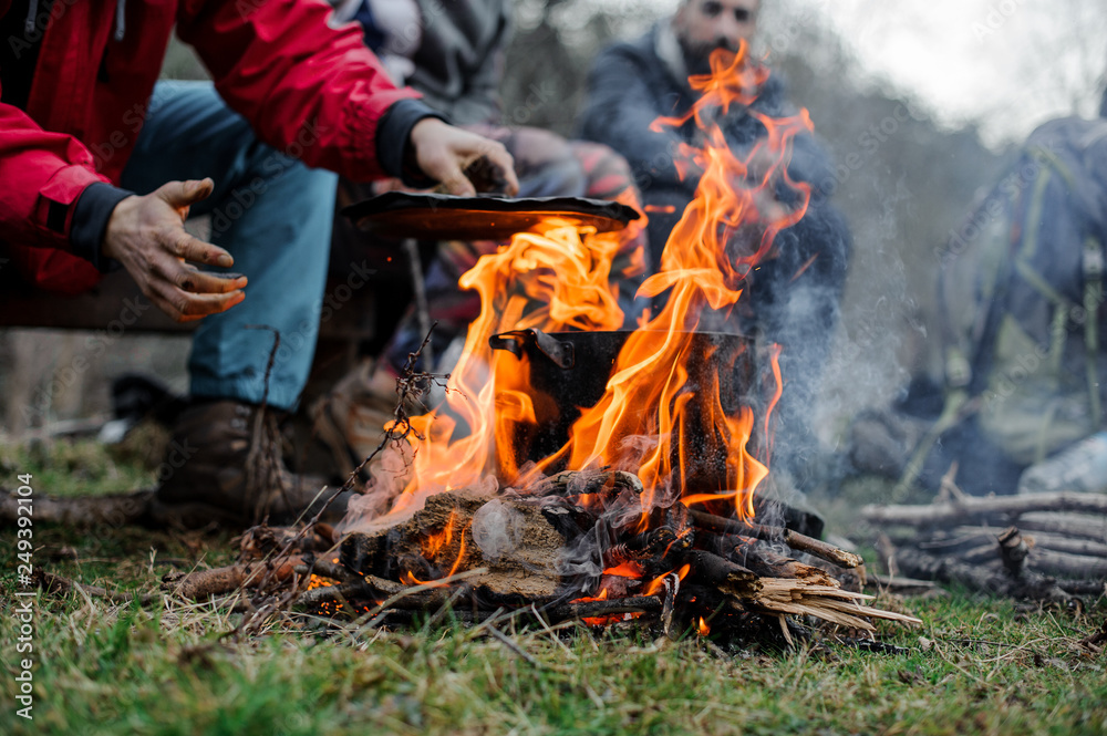 Boy in a red jacket placing a cover on the black pan standing on the bonfire Boy in a red jacket placing a cover on the black pan standing on the bonfire