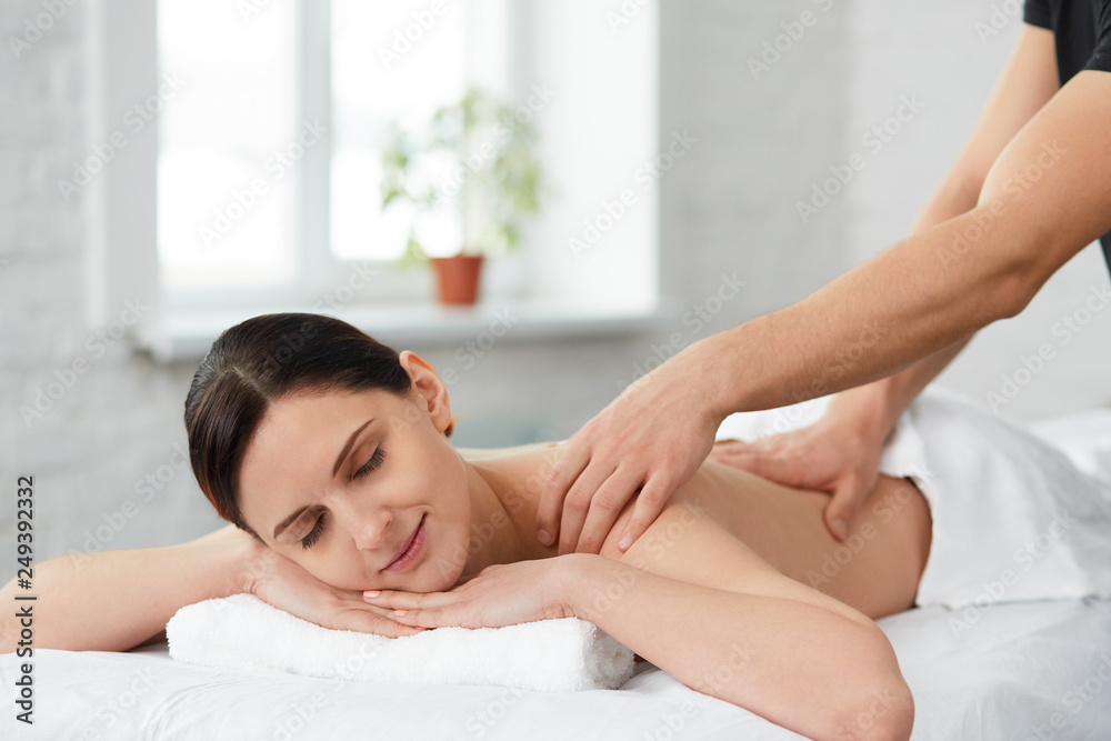 Young beautiful woman enjoying a back massage. Professional massage therapist is treating a female patient in apartment. Relaxation, beauty, body and face treatment concept. Home massage. Young beautiful woman enjoying a back massage. Professional massage therapist is treating a female patient in apartment. Relaxation, beauty, body and face treatment concept. Home massage.