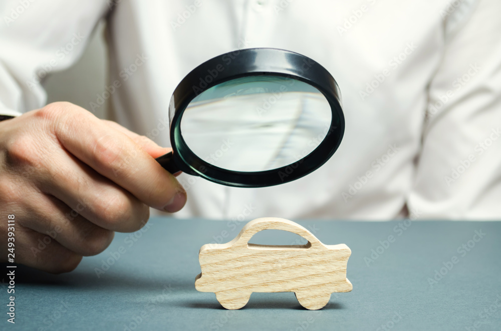 A man holds a magnifying glass over a miniature wooden car. The estimated  cost of the