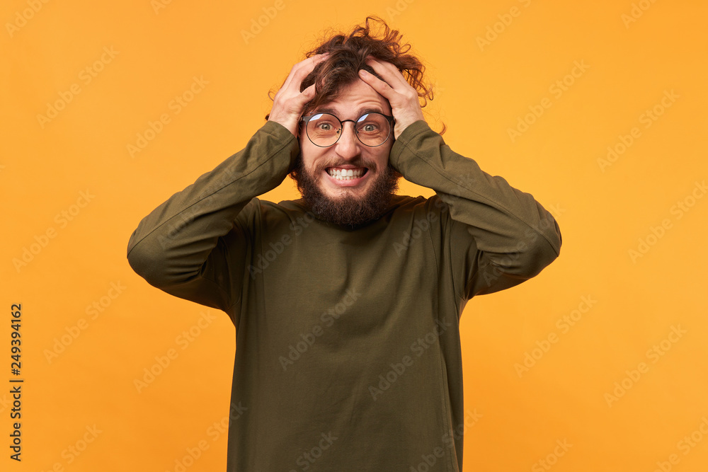 Portrait of a man in glasses with a beard clutched at his head looks glad amazed overwhelmed with emotions, surprised male, keeps mouth opened, isolated on a yellow background. Portrait of a man in glasses with a beard clutched at his head looks glad amazed overwhelmed with emotions, surprised male, keeps mouth opened, isolated on a yellow background.