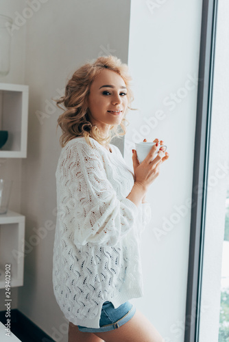 Wonderful girl in knitted sweater and denim shorts drinking coffee