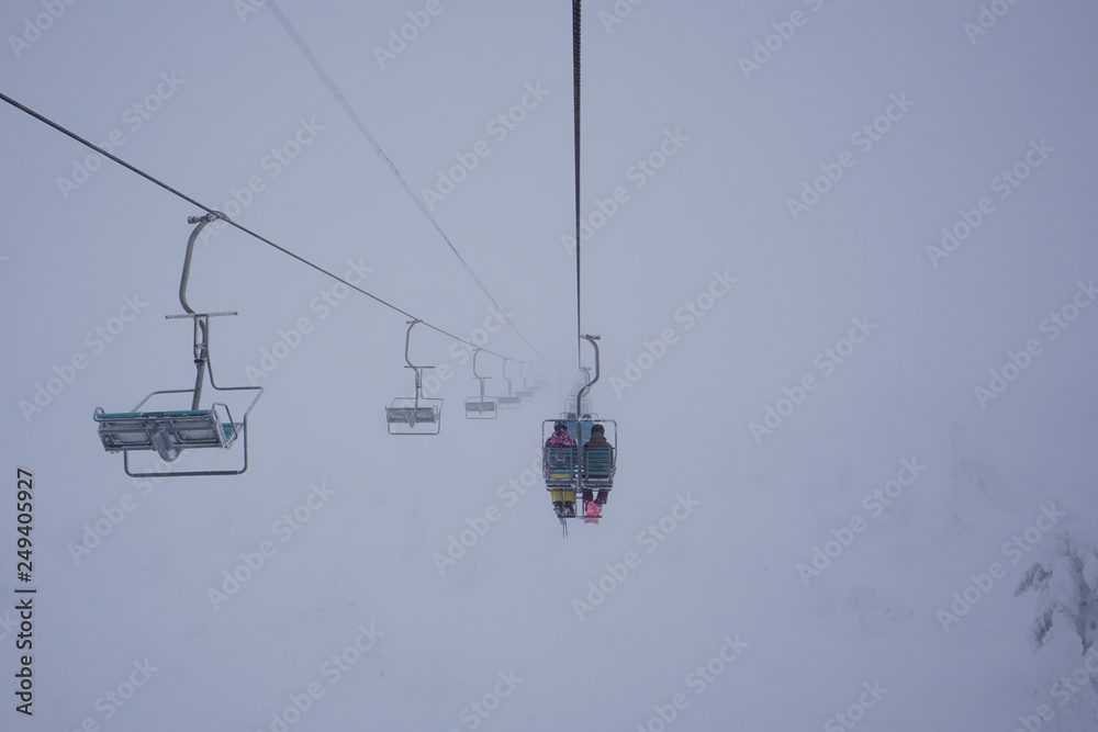Chairlift at a ski resort, with two skiers, in the fog Chairlift at a ski resort, with two skiers, in the fog
