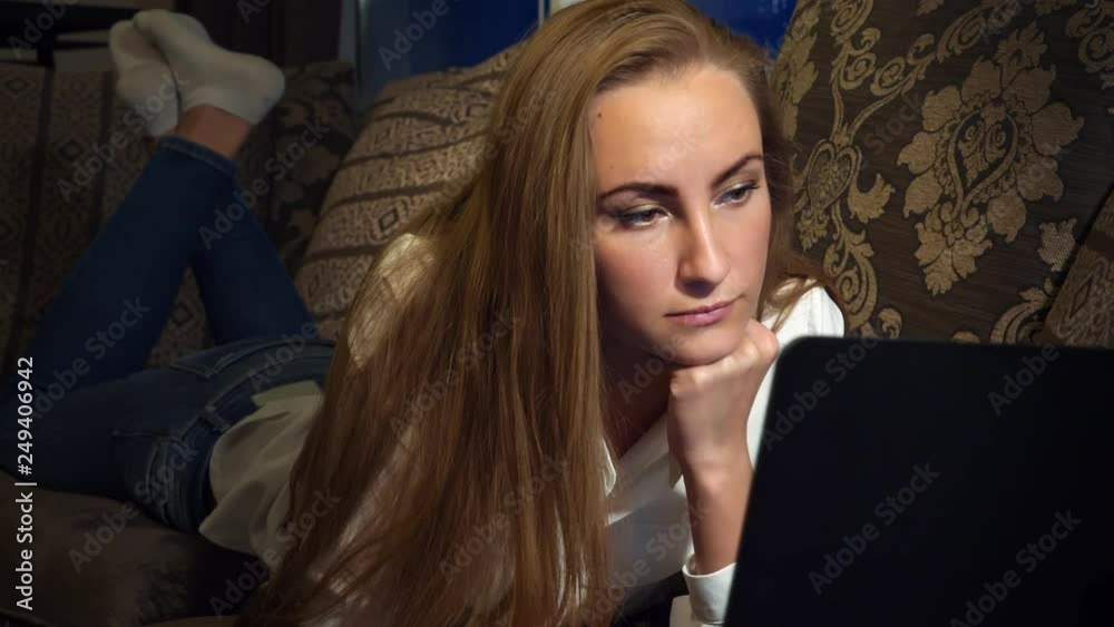 fair-haired in a white shirt business woman working on a laptop on the sofa at home by the window evening or at night dolly shot fair-haired in a white shirt business woman working on a laptop on the sofa at home by the window evening or at night dolly shot