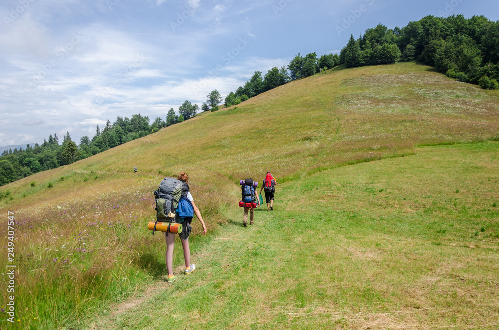 Several tourists with backpacks go along the path in the mountains