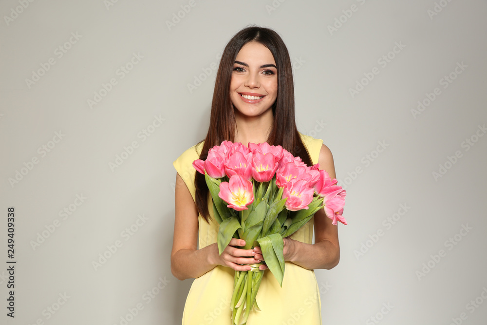 Portrait of beautiful smiling girl with spring tulips on light background. International Women's Day