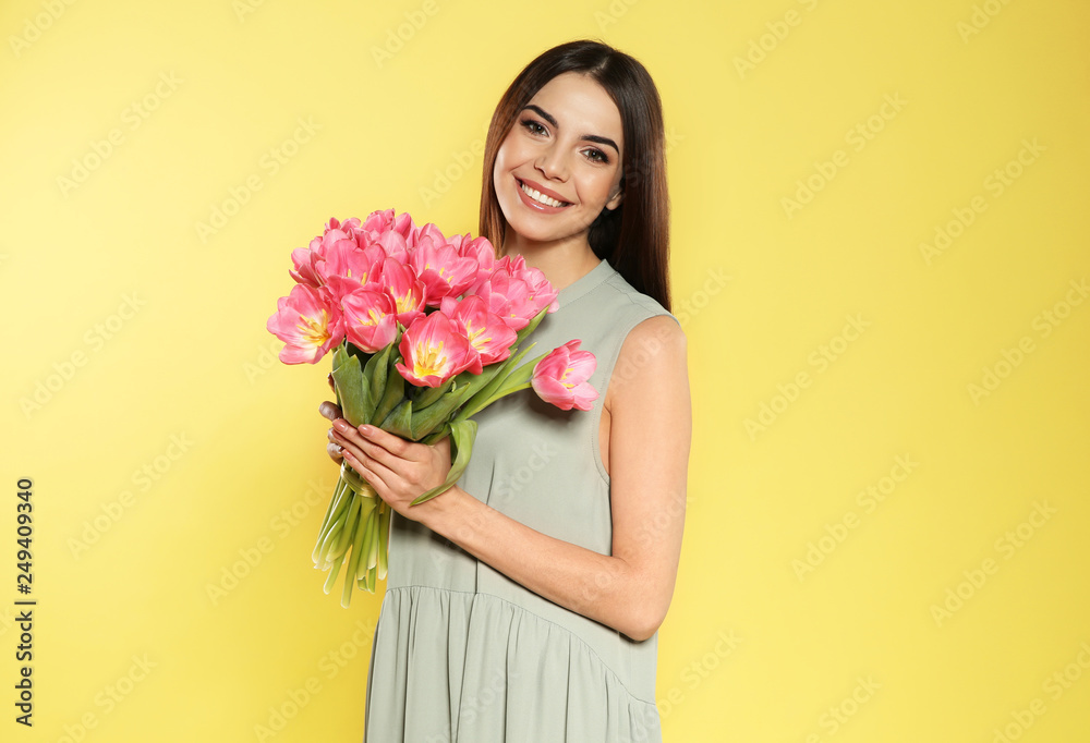 Portrait of beautiful smiling girl with spring tulips on yellow background. International Women's Day