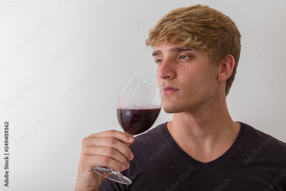 Concentrated young man sommelier with red wine in glass over white background Concentrated young man sommelier with red wine in glass over white background