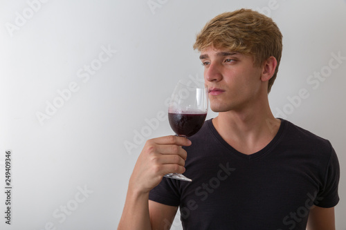 Concentrated young man sommelier with red wine in glass over white background