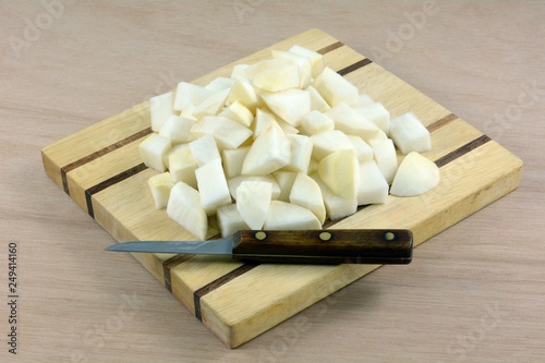 Chopped raw turnips on wooden cutting board with kitchen knife on wood table photo