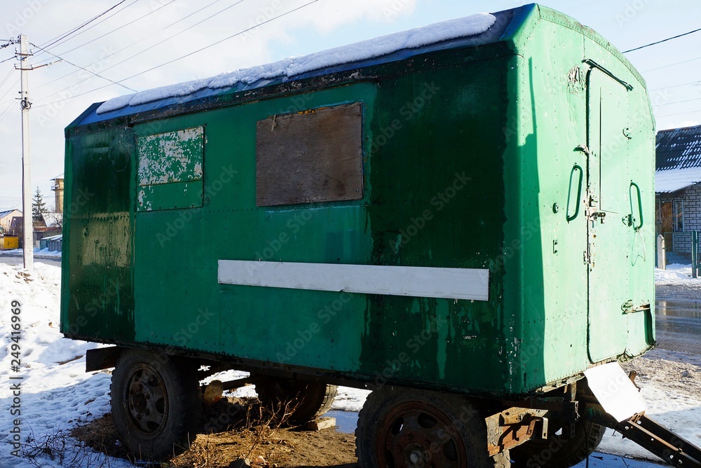 one green old metal trailer booth stands on the road in a snowdrift of white snow on a city street