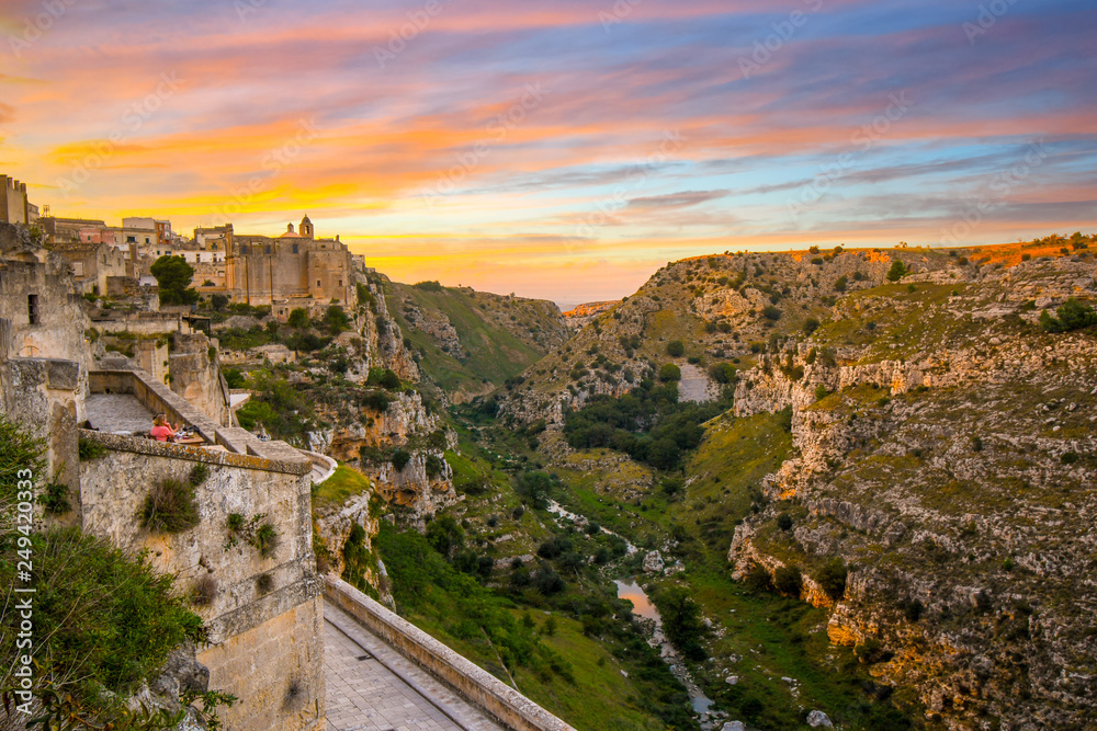 Two women enjoy a sunset meal on a terrace in the ancient city of Matera, Italy, overlooking the sassi caves, canyon ravine and the Convent of Saint Agostino