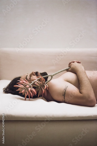 Side view of shirtless man with flower laying on couch