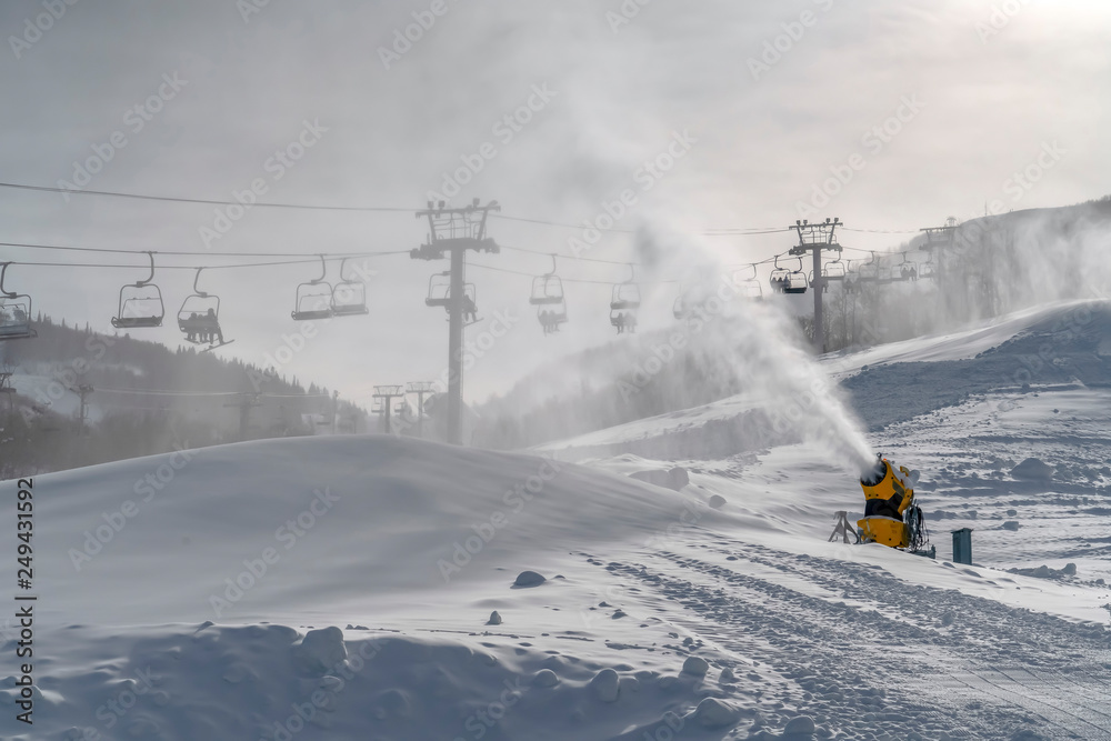 Skiers on ski lifts overlooking a snow cannon Skiers on ski lifts overlooking a snow cannon