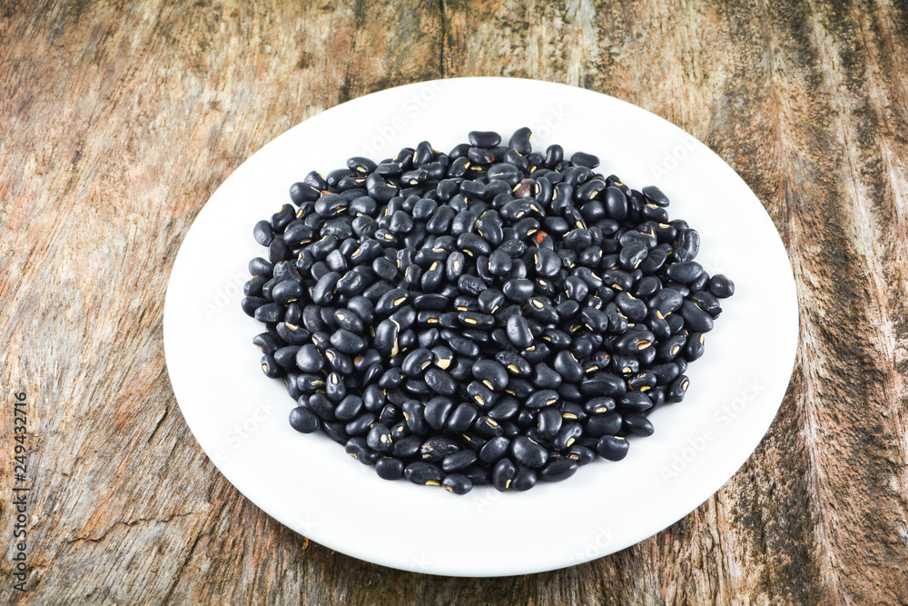 Black bean grain seeds on white plate food on wooden background Black bean grain seeds on white plate food on wooden background