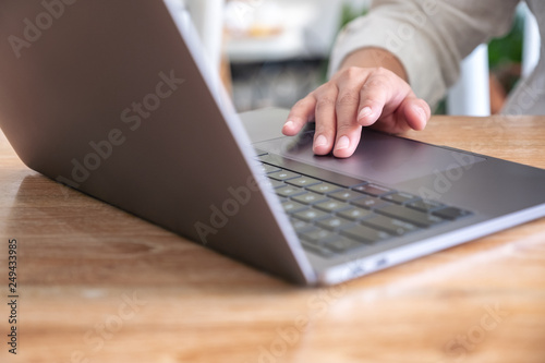 Closeup image of hand using and touching on laptop touchpad on wooden table