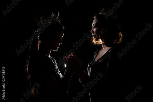 Two Silhouette Shadow Back Rim Light of Miss Pageant Beauty Queen Contest with Silver Diamond Crown hold pray together for final moment announce Winner prize, studio lighting dark black background
