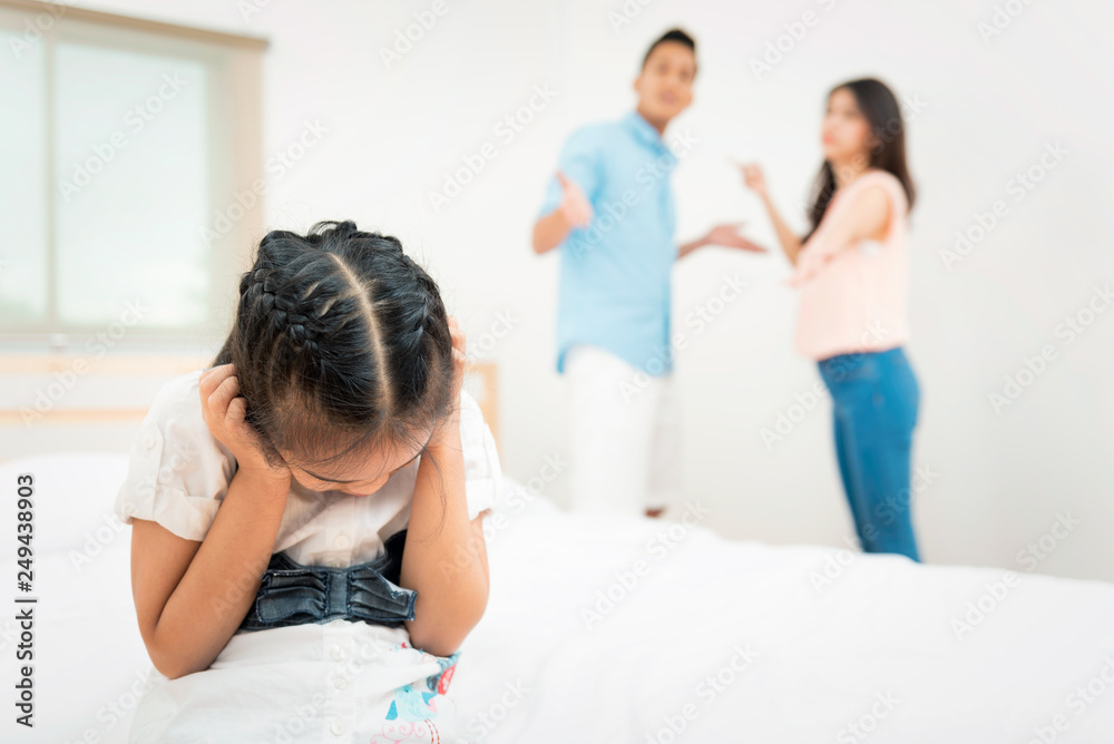Family problem and child with background at quarrel of parents. Sad little girl is unhappy while in the bed room and cry against arguing parents at home or Conflict happened in the family Family problem and child with background at quarrel of parents. Sad little girl is unhappy while in the bed room and cry against arguing parents at home or Conflict happened in the family