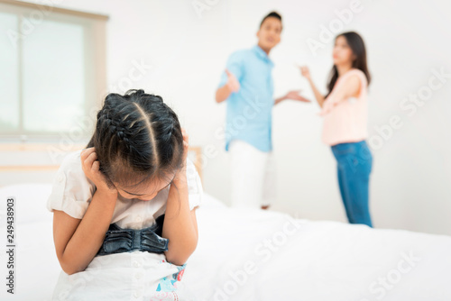 Family problem and child with background at quarrel of parents. Sad little girl is unhappy while in the bed room and cry against arguing parents at home or Conflict happened in the family