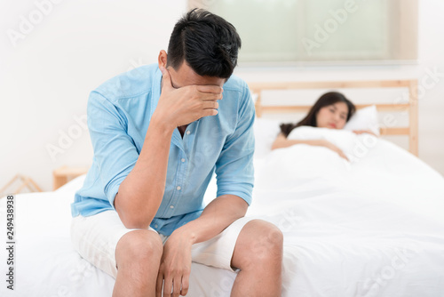 Husband unhappy and disappointed in the erectile dysfunction during sex while his wife sleeping on the bed. Sexual Problems in Men.