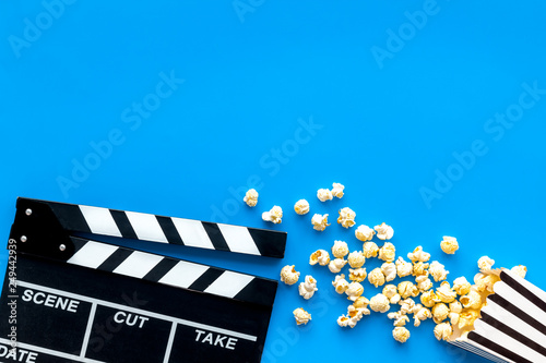 Film watching concept. Clapperboard and popcorn on blue background top view copy space