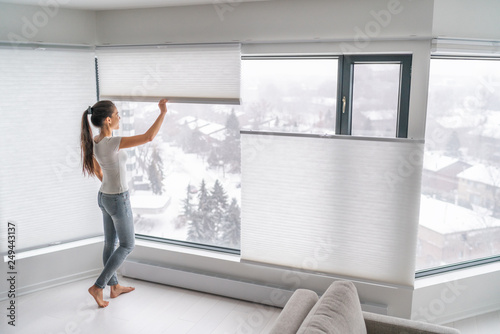 Woman opening home curtains in urban condo. Modern top down bottom up privacy cellular shades on apartment window keeping heat in winter with honeycomb blind curtain. Cordless pleated shades.