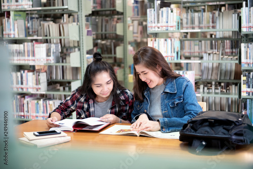 Two Asian female students open reading a magazine and Smiling Relaxation in the Public library. Life of studying and friendship in International College/University.