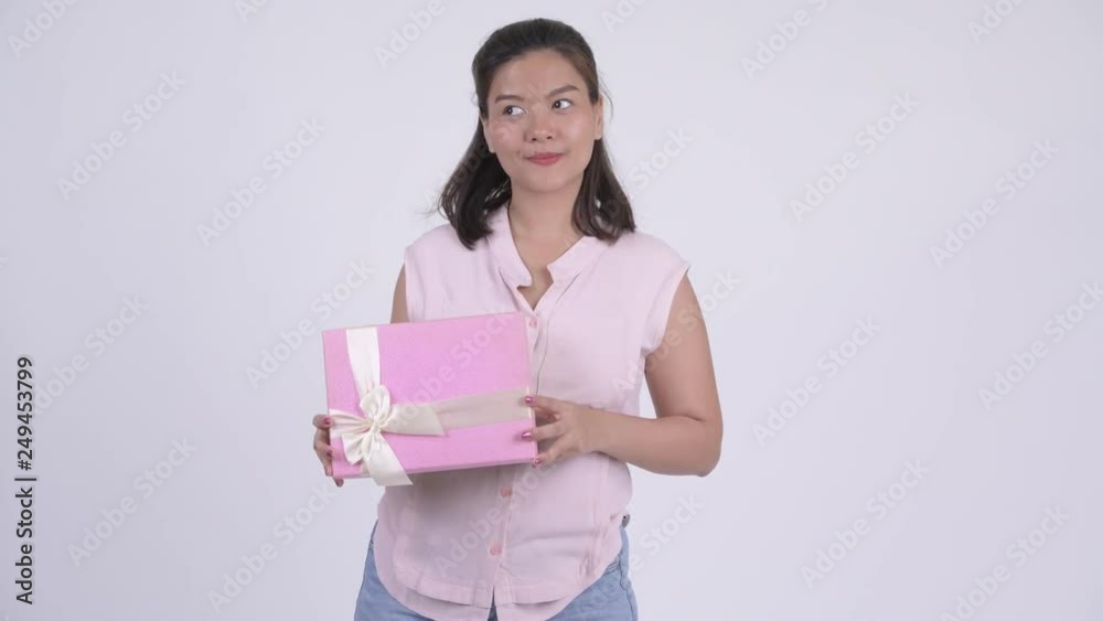 Young happy Asian businesswoman thinking while holding gift box Young happy Asian businesswoman thinking while holding gift box