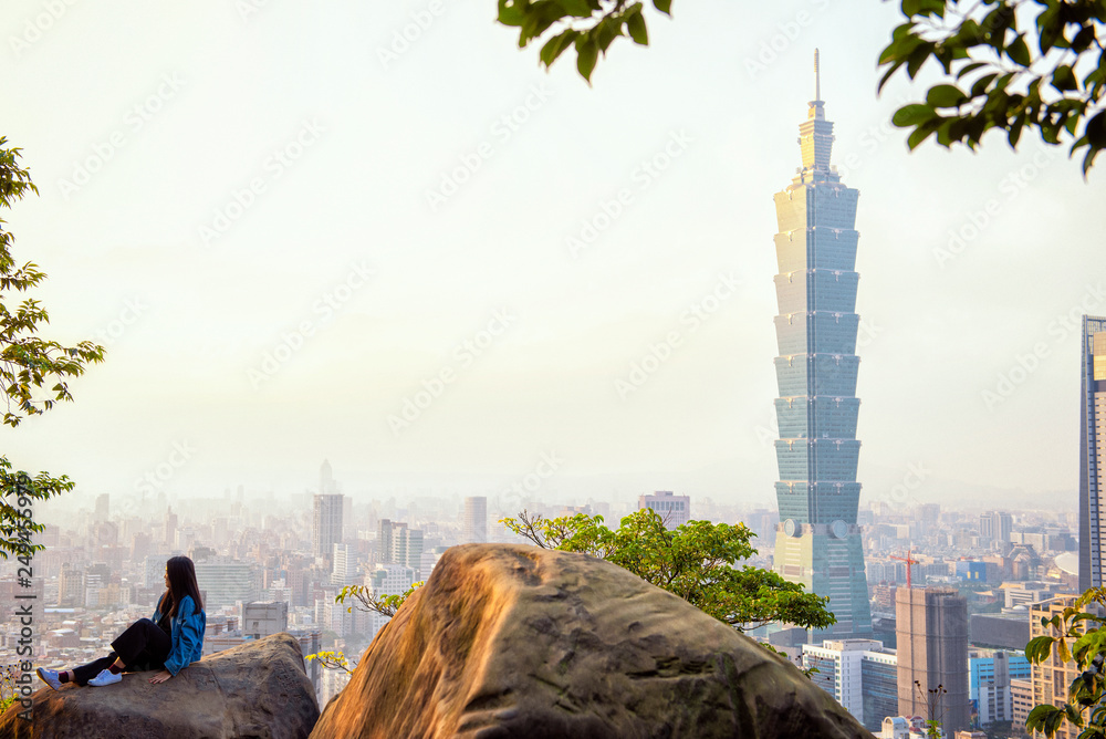 Fototapeta premium Taipei, Taiwan - January 25, 2019: tourist woman sit on giant stone with 101 tower at sunset