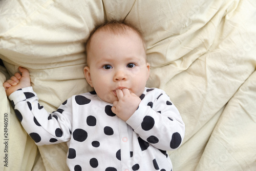 portrait of a kid with fingers in his mouth. little baby in bed sucks her fingers