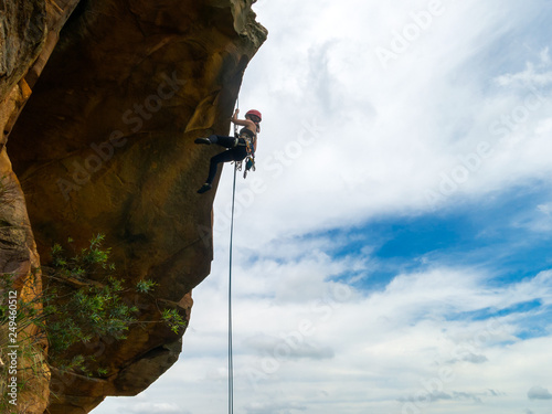 Abseiling a negative sanstone rock wall with blue sky on background