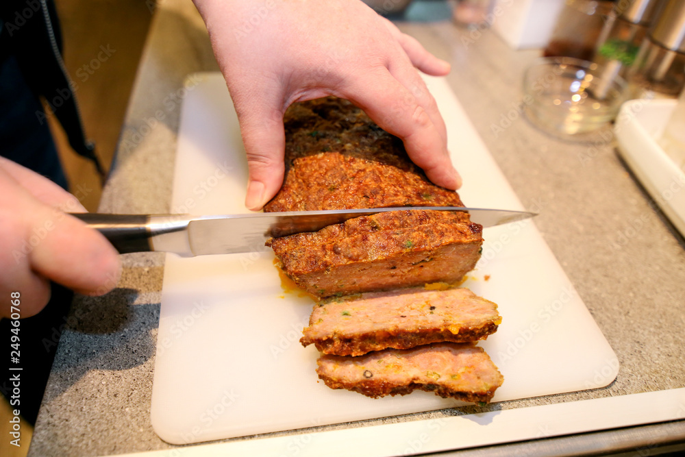 Woman hands cutting piece of meatloaf, she prepare for tasting of food at kitchen. Chef cutting meatloaf with knife on board on restaurant kitchen table. Housewife sliced meatloaf on cutting board.