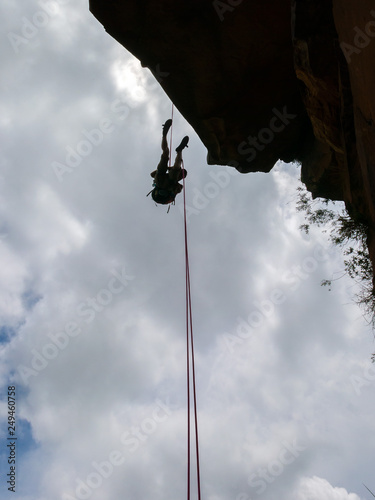 Abseiling a negative sanstone rock wall with blue sky on background - view from bellow photo