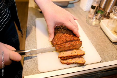 Woman hands cutting piece of meatloaf, she prepare for tasting of food at kitchen. Chef cutting meatloaf with knife on board on restaurant kitchen table. Housewife sliced meatloaf on cutting board.