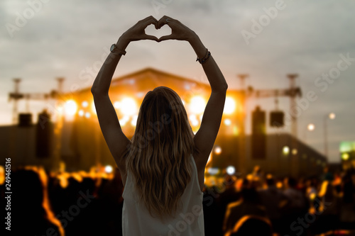 Girl with heart-shape symbol enjoying her favorite group on the concert.