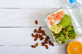 Lunch box: rice, salmon, salad with cucumber, avocado, greens on a white wooden background. Fitness food. The concept of healthy eating. School lunch box