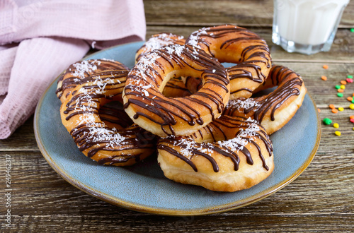 Homemade classic donuts with chocolate and coconut flakes on a wooden background.