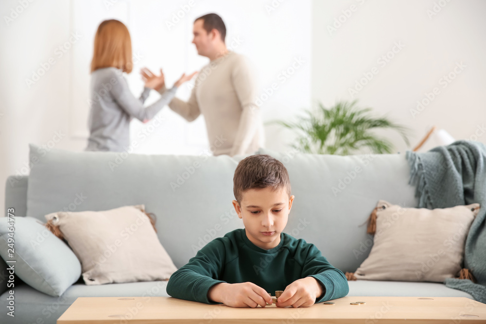 Sad little boy with coins and his quarreling parents at home. Concept of child support Sad little boy with coins and his quarreling parents at home. Concept of child support