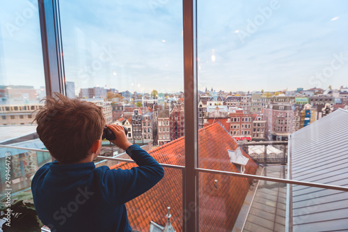 Child with binoculars looking at colorful roofs and buildings of Amsterdam from above, travel destination concept with copy space photo