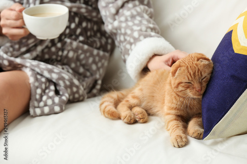 Young woman with cute funny cat drinking coffee at home