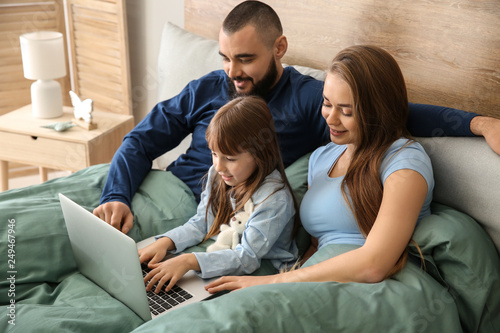Happy family with laptop on bed at home