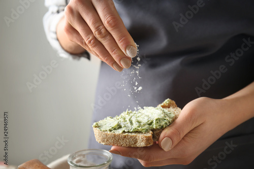 Obraz na plátně Young woman sprinkling cheese onto piece of fresh bread with green butter, close