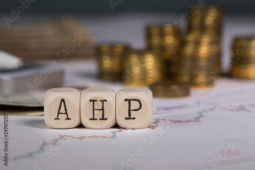 Abbreviation AHP composed of wooden letter. Stacks of coins in the background.