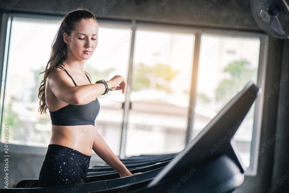Attractive pretty Caucasian woman running on treadmill and check heart rate with smart watch at gym. Attractive pretty Caucasian woman running on treadmill and check heart rate with smart watch at gym.