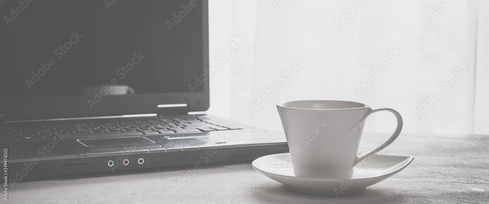 cup of coffee and a laptop on a table near a window in Scandinavian style minimalism in gray with a copy space