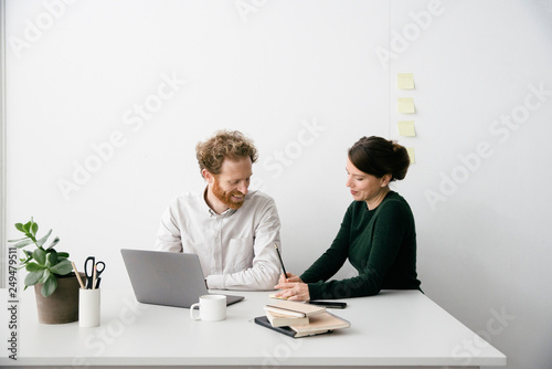A thirty something couple is working on a laptop in a clean white empty office setting.