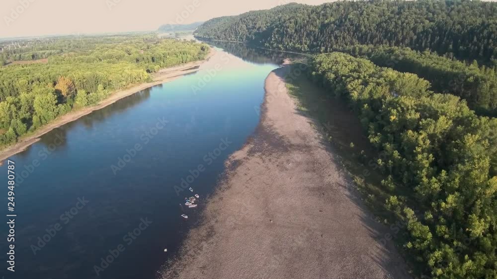 video from the drone. The rocky shore of the blue river. Mountains are visible in the distance. Boats on the water. Reflection of mountains in the water. Summer landscape Beautiful countryside. 